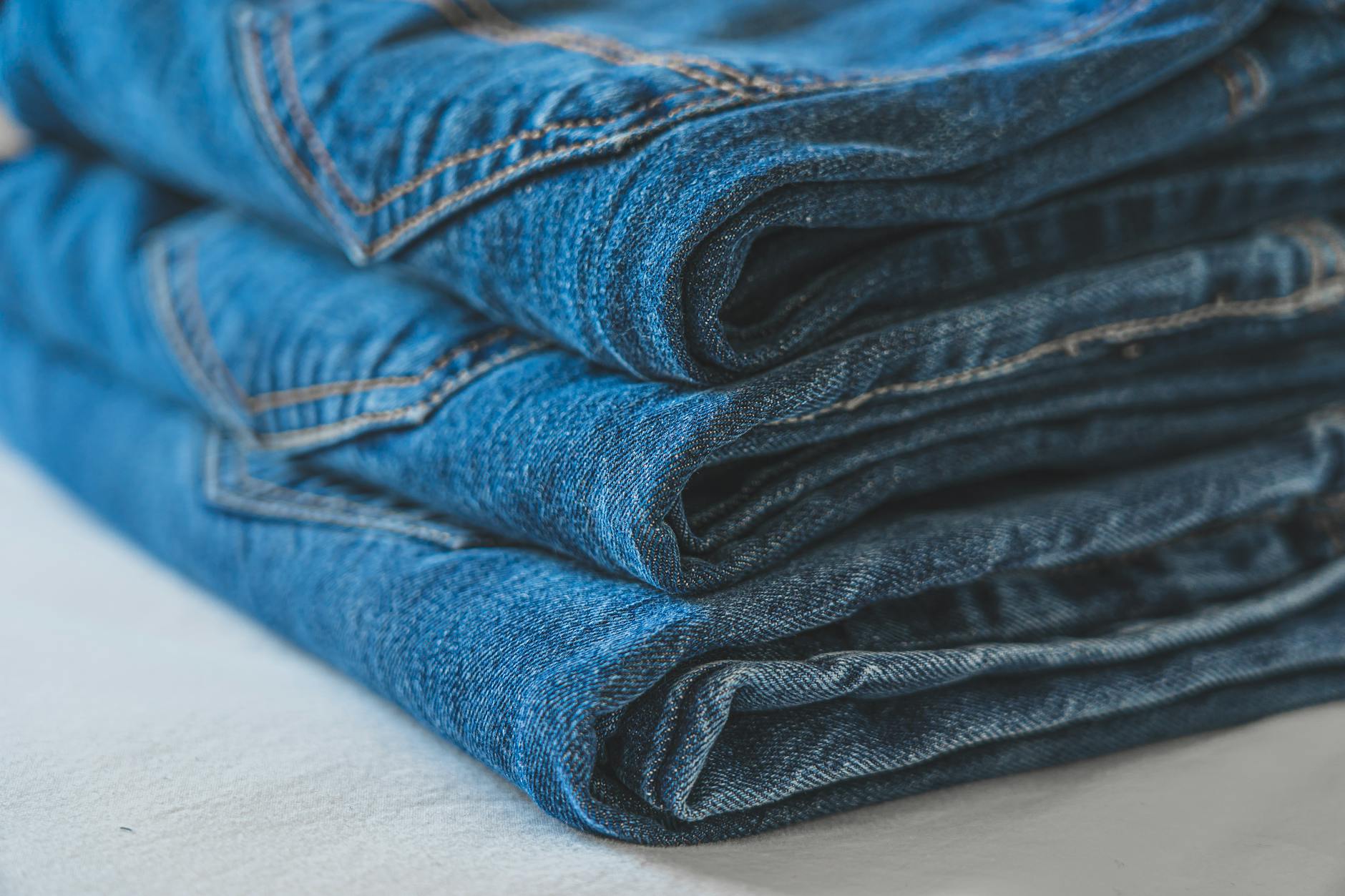 Stack of neatly folded blue denim jeans showcasing texture and stitching.