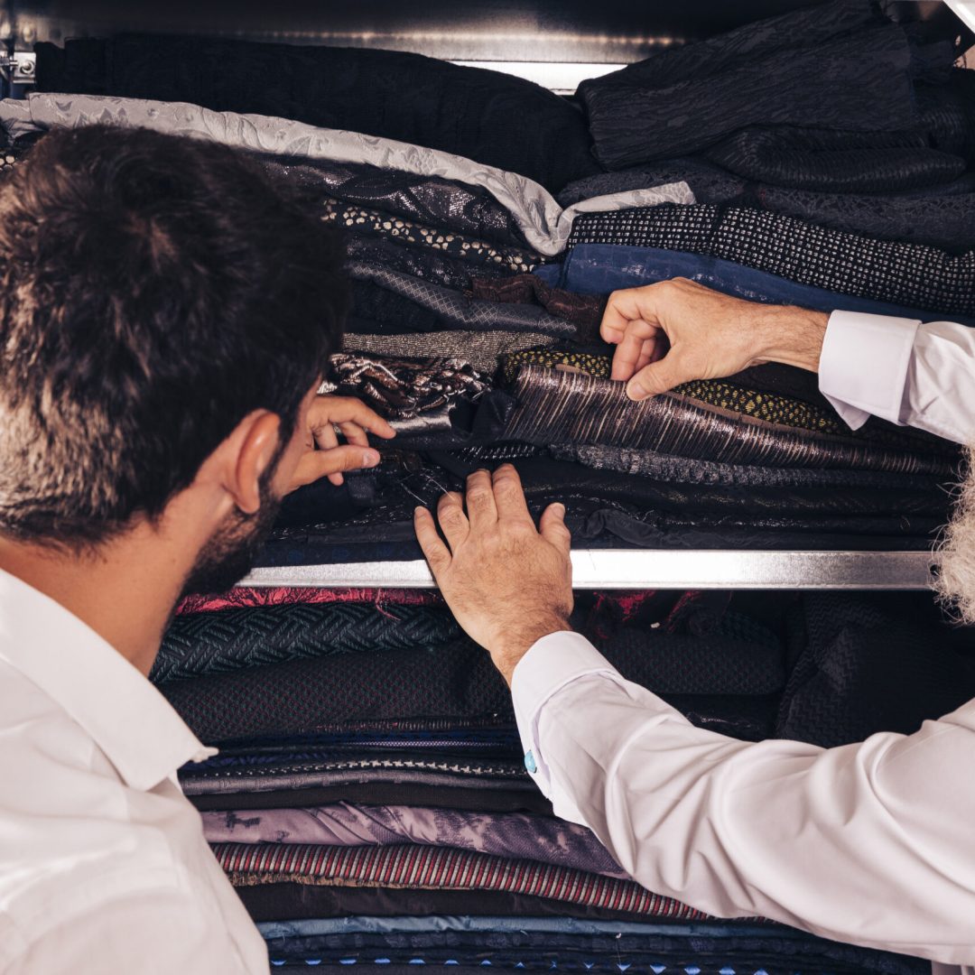 close-up-man-male-senior-tailor-selecting-fabric-shelf