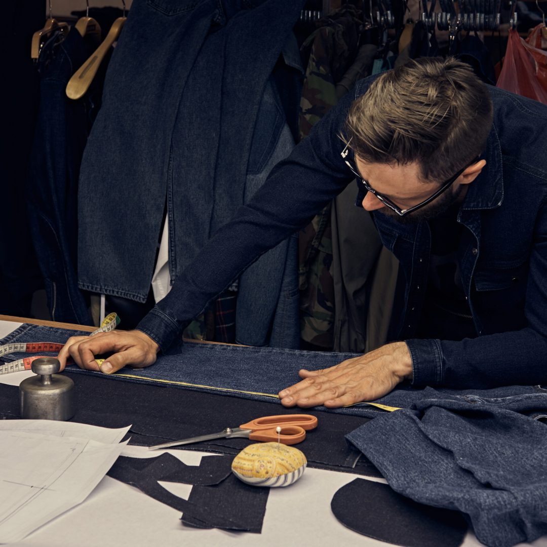 Handsome bearded tailor working with cloth samples at a sewing workshop.