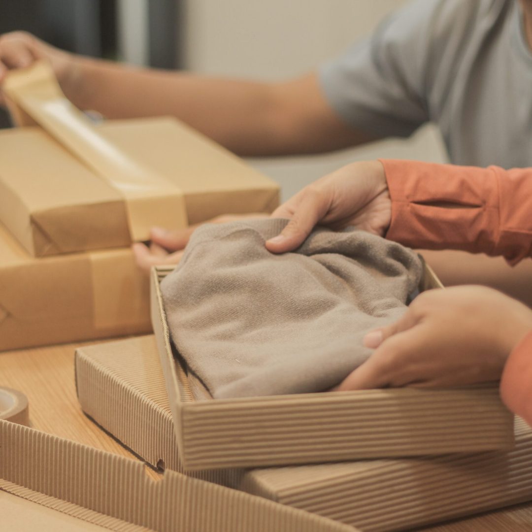 Two people putting clothes inside boxes and wrapping them
